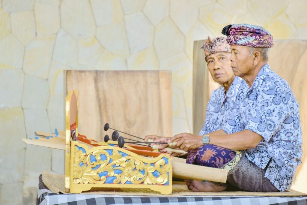 Two elderly Balinese musicians in udeng headcloths playing a gilded gender, the instrument that accompanies shadow puppet performances