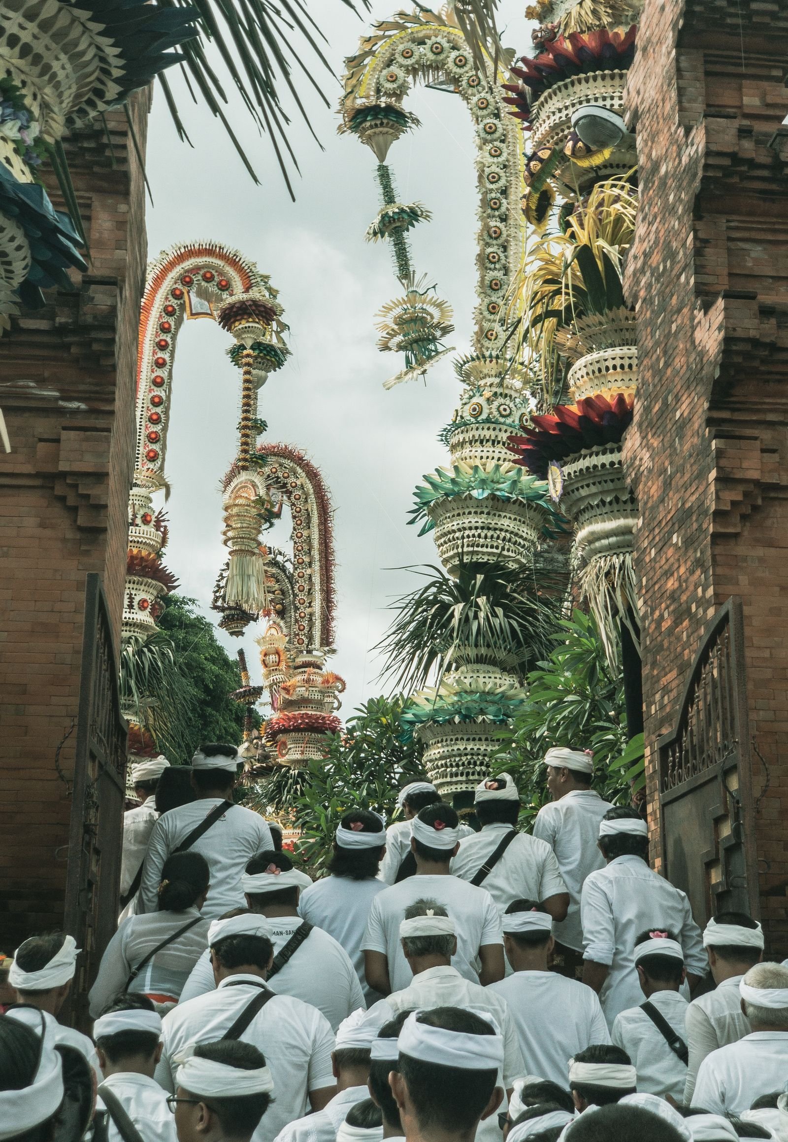 Crowds of Balinese worshippers dressed in white entering a temple gate decorated with tall penjor and offerings